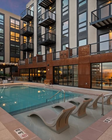 Outdoor community pool courtyard with lounge seating, string lights, and balconies at dusk
