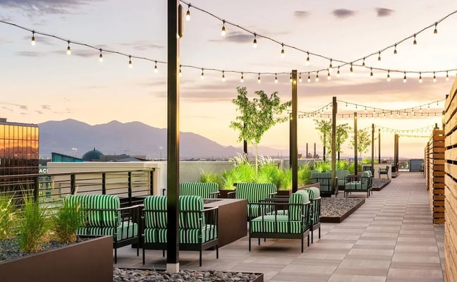 Rooftop patio with green striped chairs, string lights, and mountain and water views at dusk