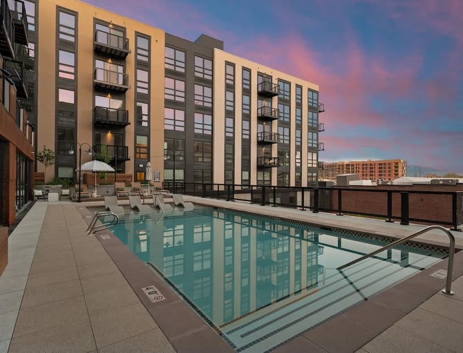 Rooftop pool with lounge chairs overlooking modern apartment buildings at sunset